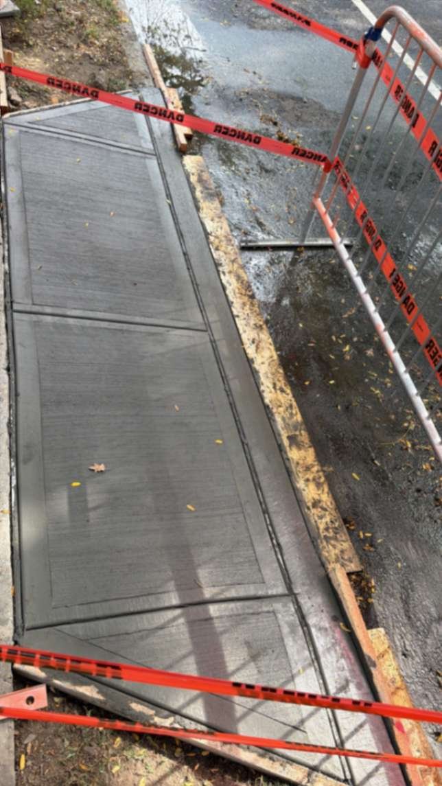 Replacement concrete sidewalk slabs along the curb after DOT violation removal in Brooklyn