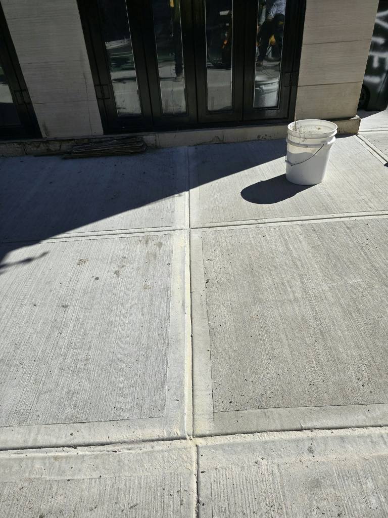 Broom-finished sidewalk flags in front of a storefront, DOT violation removal in Yorkville, NYC