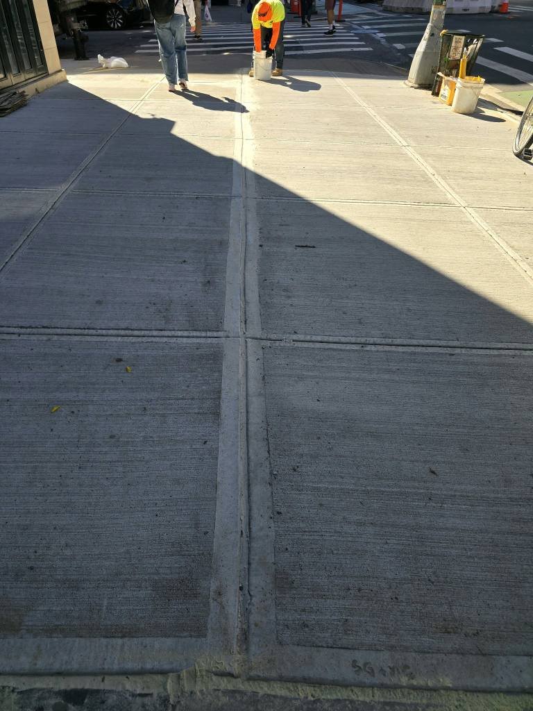 Crew finishing new sidewalk flags near a crosswalk for DOT violation removal, Upper East Side, NYC
